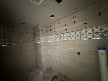 Walk-in shower tile installation with decorative mosaic accent band in progress