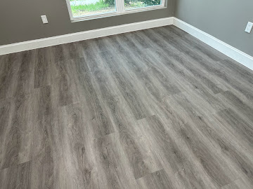 Close-up of finished grey wood-look flooring installation with white baseboard
